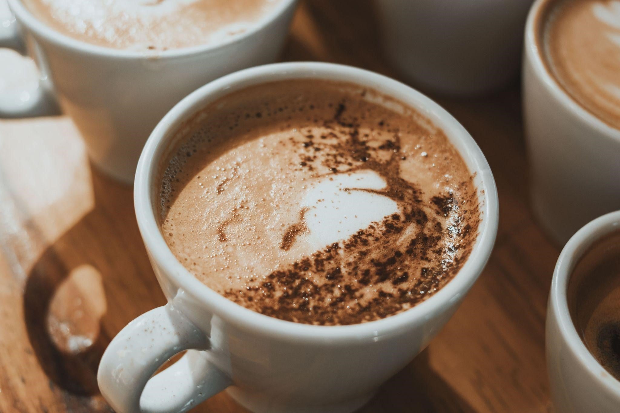 Cappuccino in a white coffee cup with a rich layer of microfoam and a sprinkle of chocolate powder.