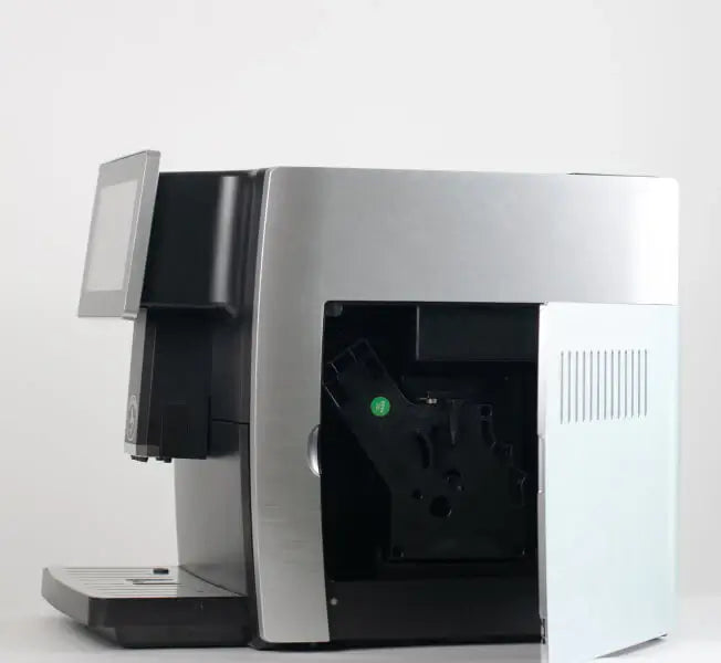 Cafe Bueno super automatic espresso machine side panel open showing removable brew group mechanism for cleaning and maintenance, brushed stainless steel body with touchscreen display visible, white studio background.